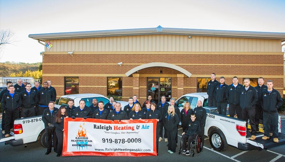 Raleigh Heating & Air staff standing outside building with service trucks and a large banner.