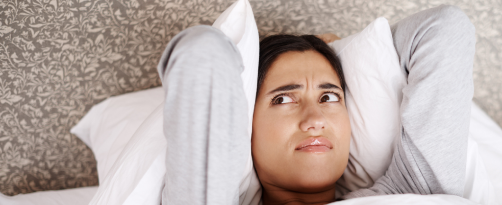 Stock photo of a woman covering her ears with a pillow from canva for our Why Does My Furnace Smell post.